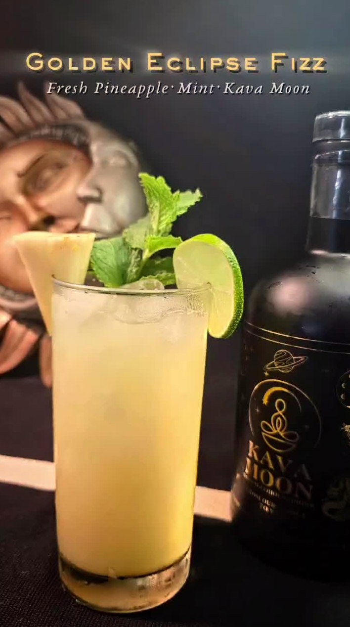 Golden Eclipse Fizz kava mocktail in a tall glass with pineapple, mint and a lime wheel, next to a Kava Moon bottle
