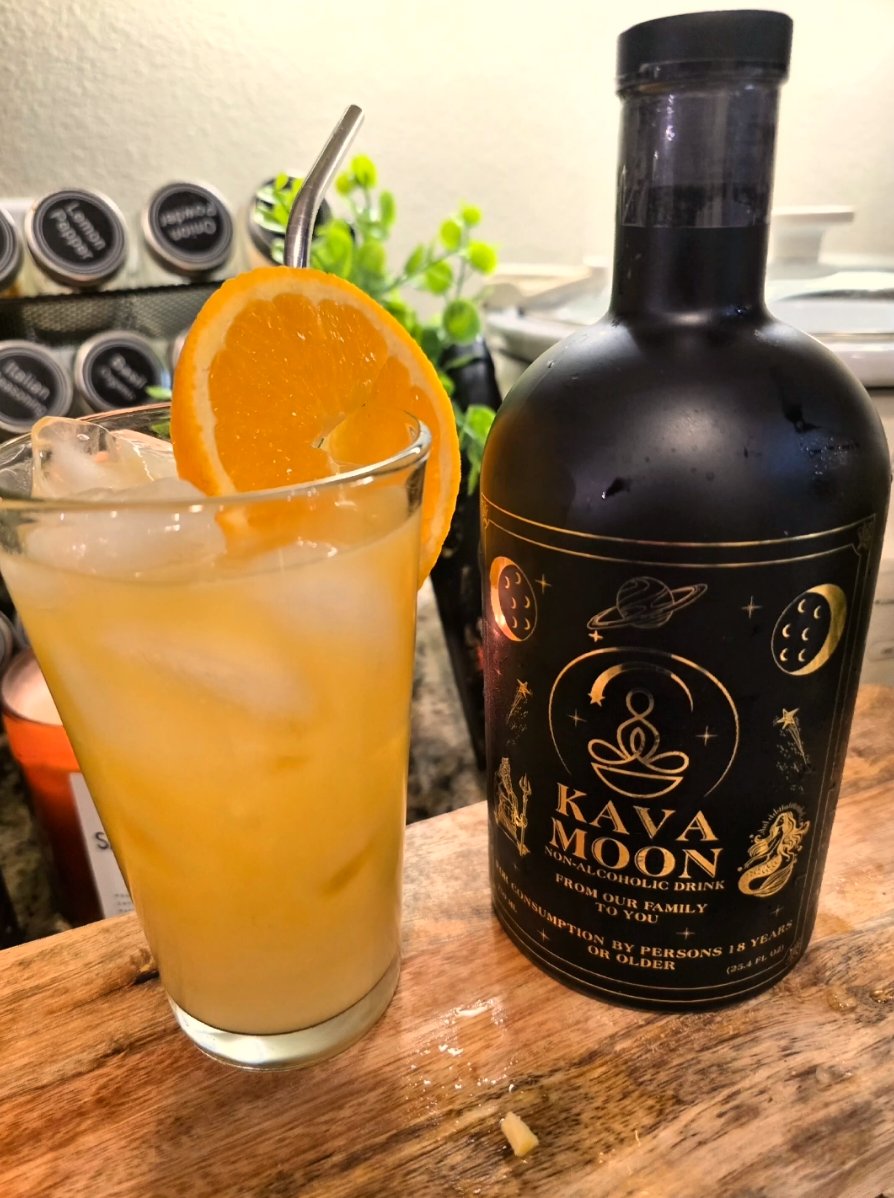 Kava Moon orange smoothie over ice with an orange wheel garnish, next to a Kava Moon bottle on a wooden board